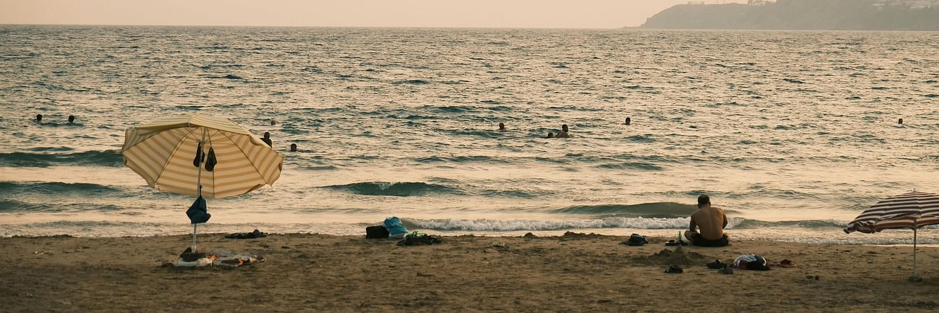 Beach scene at sunset with people enjoying seaside activities along sandy shoreline and gentle waves