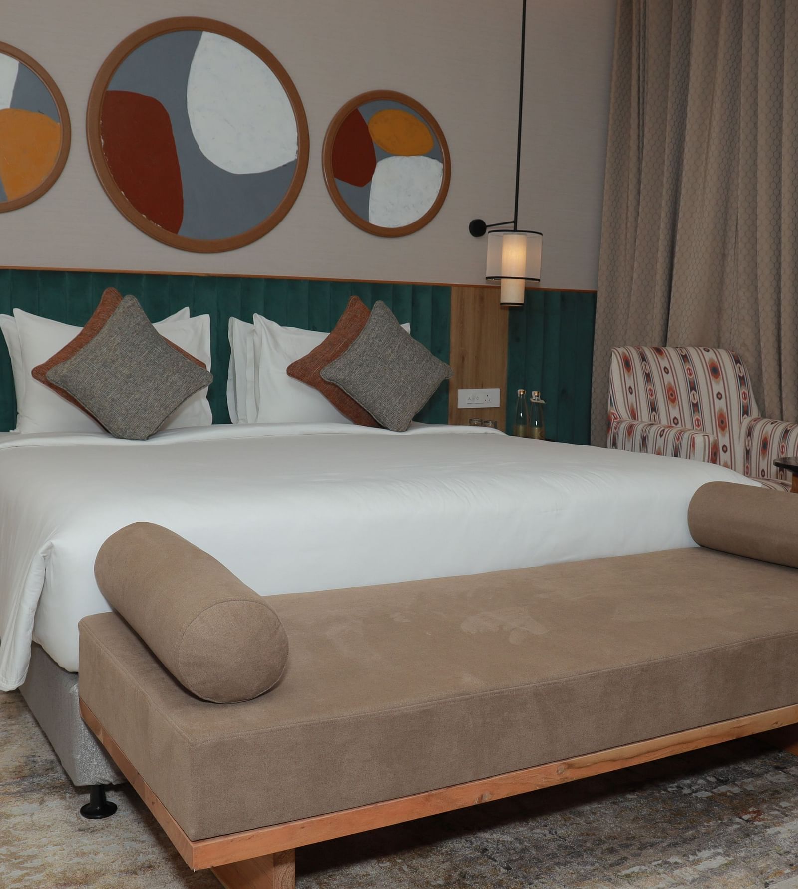A bed with a bench and a beautiful wall painting above the headboard in our suite at Regency Tuticorin - Thoothukudi Hotel Rooms
