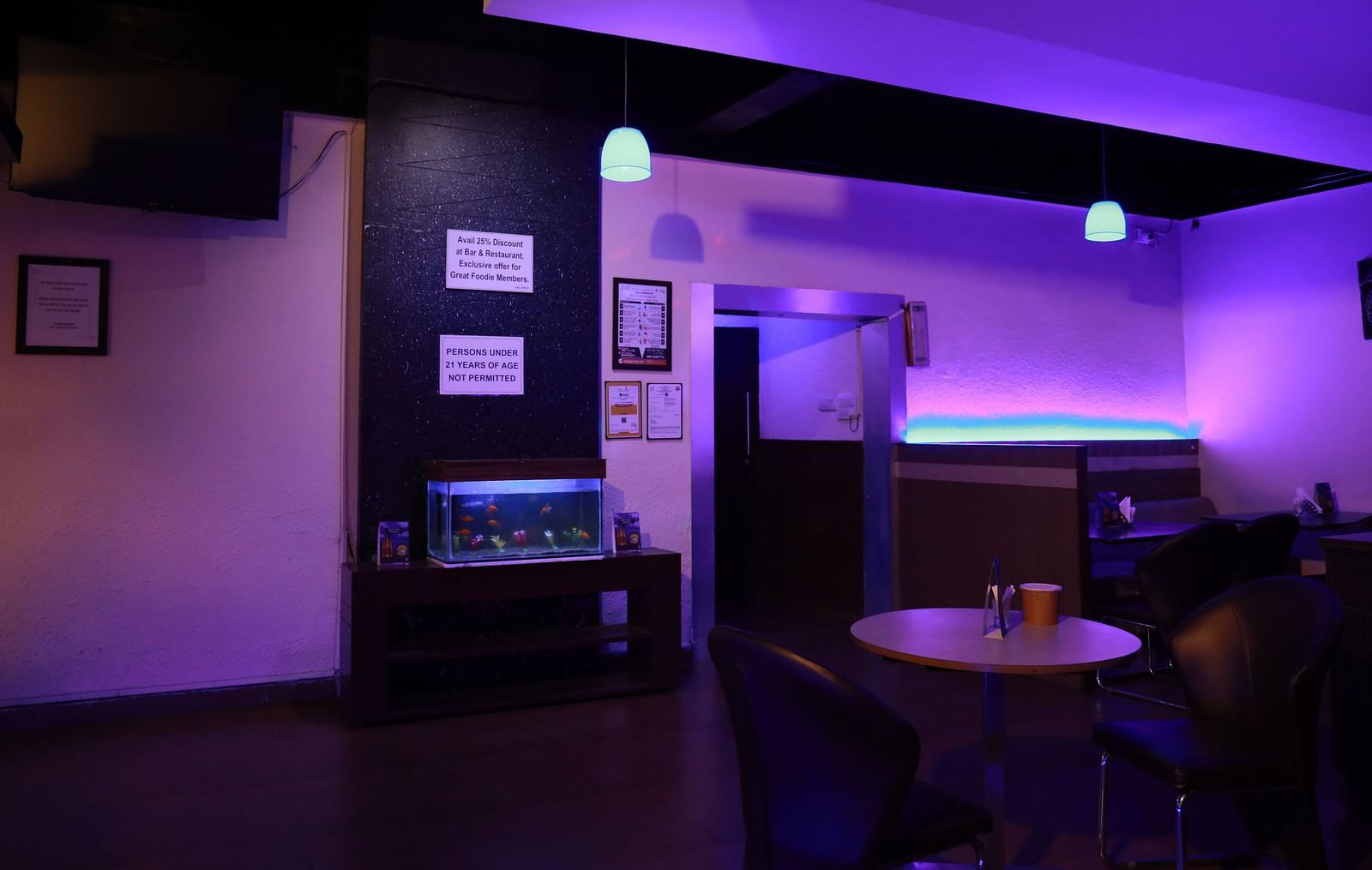 An image of a corner space in our moodily lit bar, featuring discounts displayed on the wall above a fish tank - Regency Tuticorin by GRT Hotels