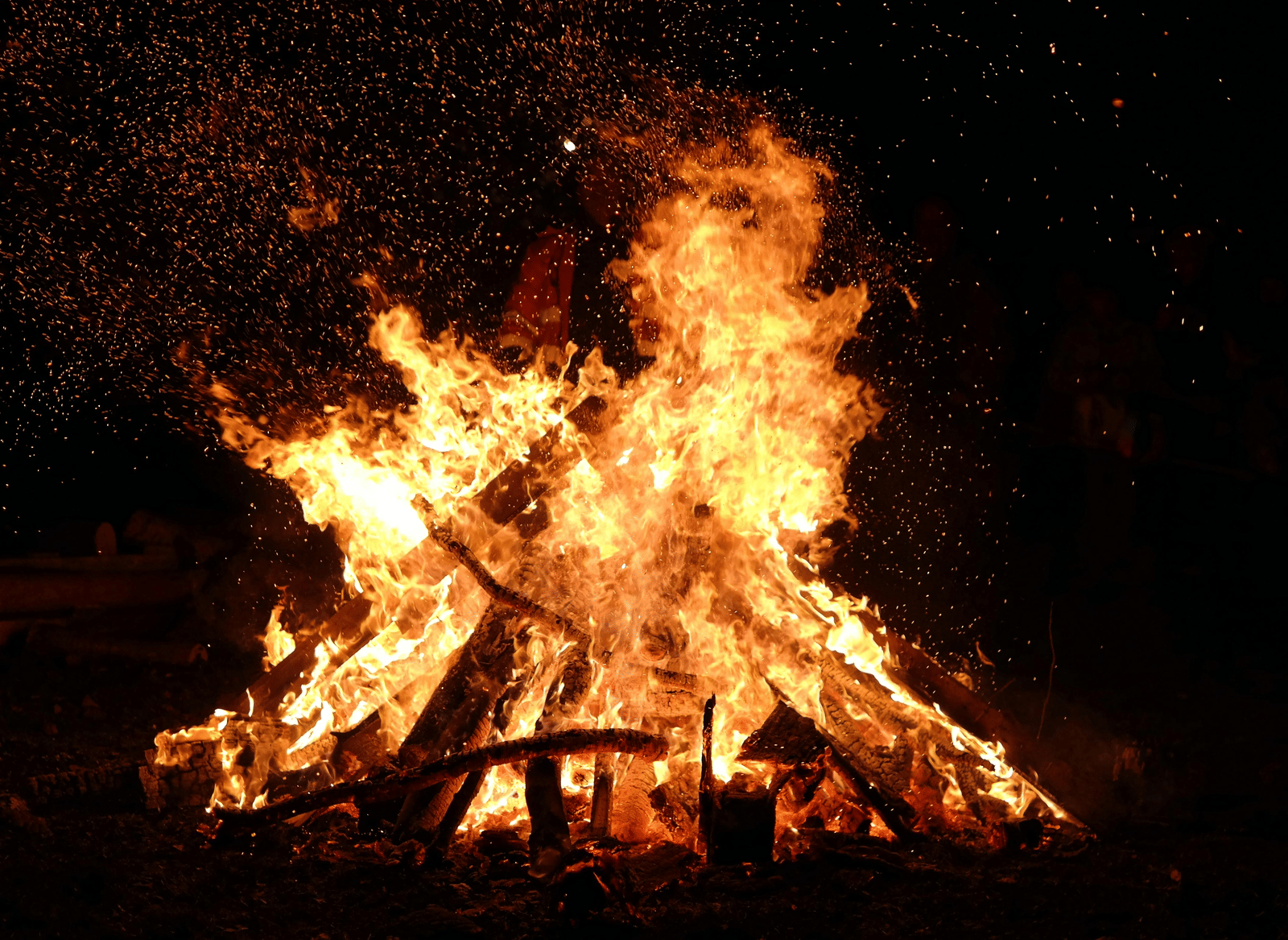 A large bonfire burning brightly at night with glowing flames and flying sparks.