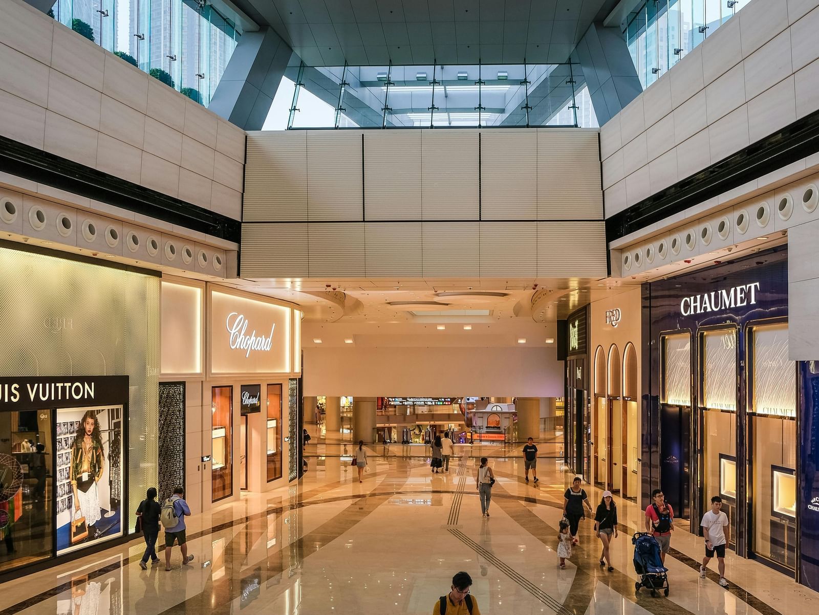 Modern shopping mall interior with branded stores, glass ceiling and bright lighting.