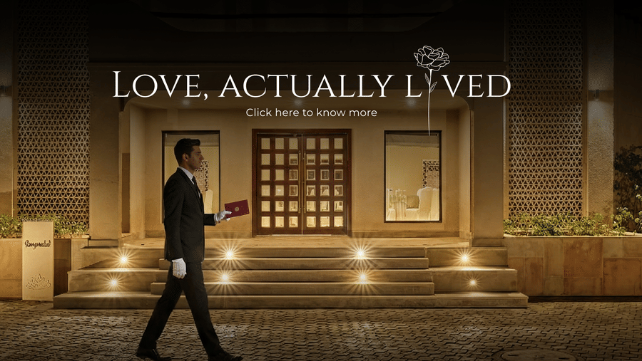 Elegant hotel entrance at night with warm lighting and a staff member walking past, showcasing the “Love, Actually Lived” romantic experience.