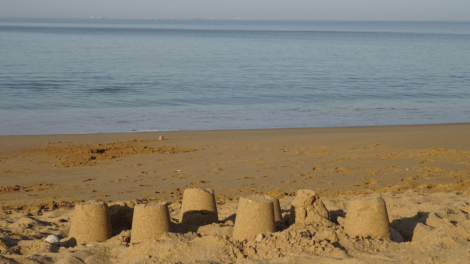 An overview of sandcastles on the beach made by people with waves in the background.