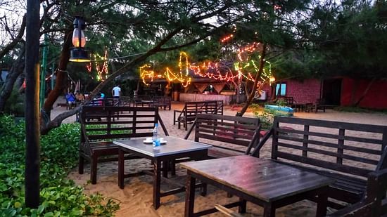 A seating area with two tables in the centre, surrounded by lush trees and plants, offering a tranquil setting at Lotus Eco Beach Resort, Konark.