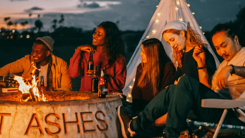 A group of friends sits together at a bonfire with the word 'ashes' written on it.