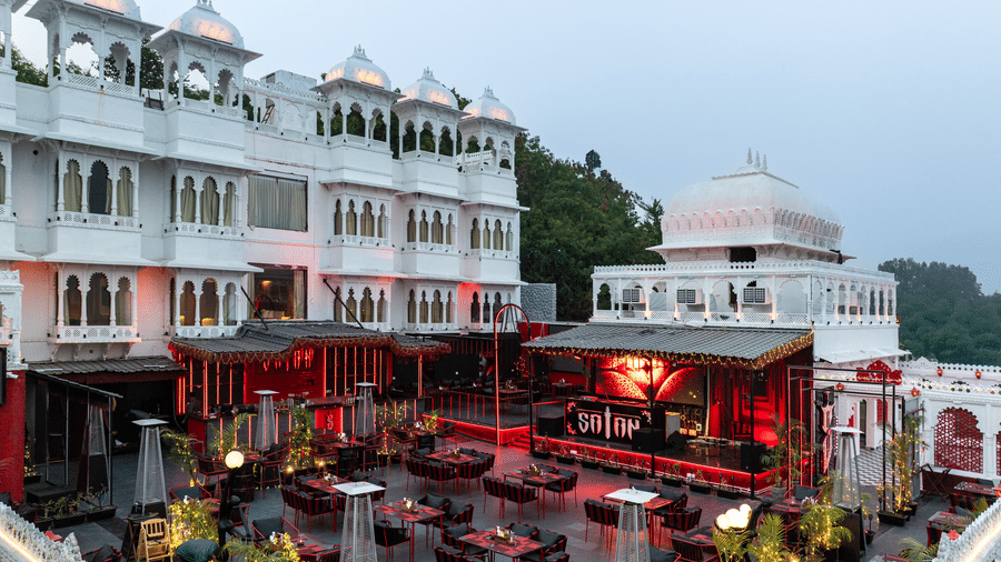 Hotel rooftop bar area with red seating and a low-lit atmosphere, set against a white heritage building exterior.