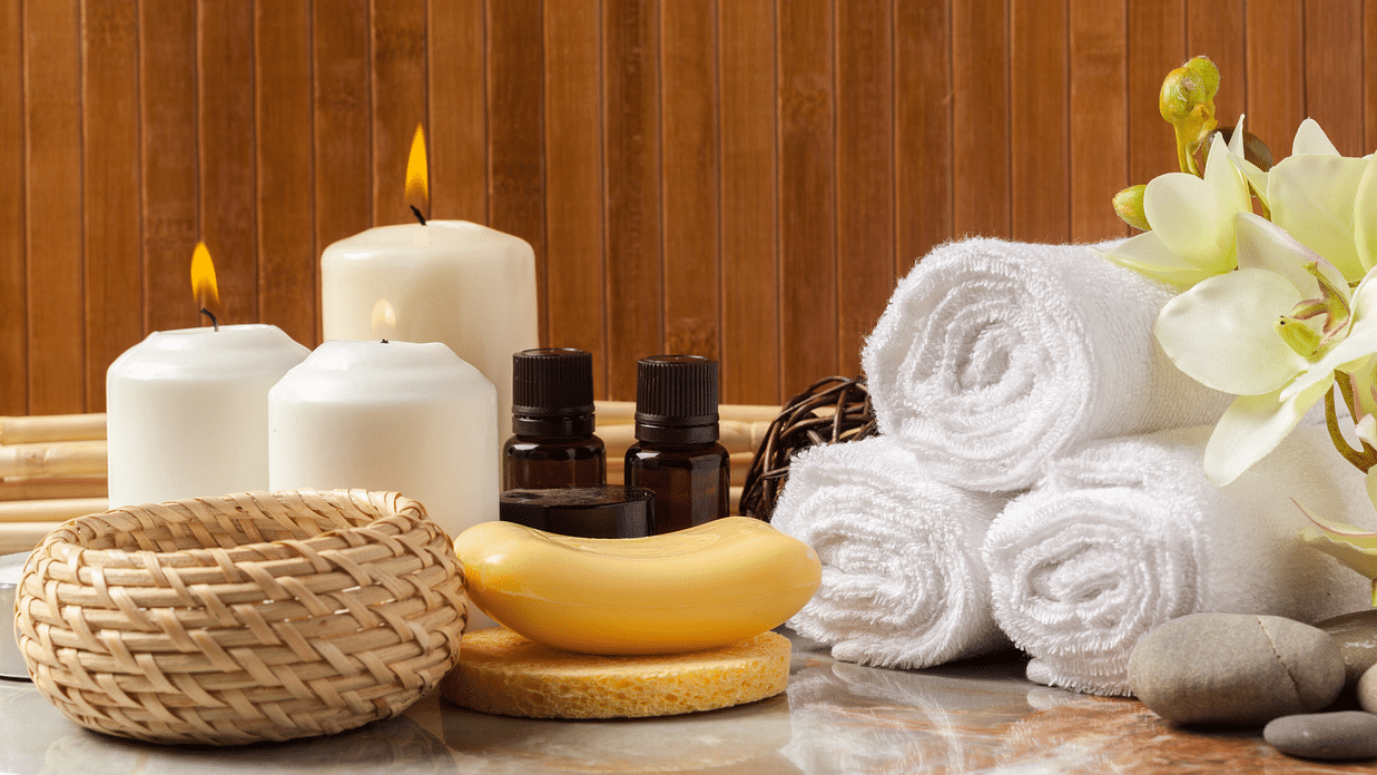 Image of towels beautifully wrapped and placed next to candles and two bottles of essential oils
