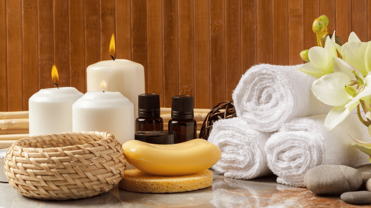 Image of towels beautifully wrapped and placed next to candles and two bottles of essential oils