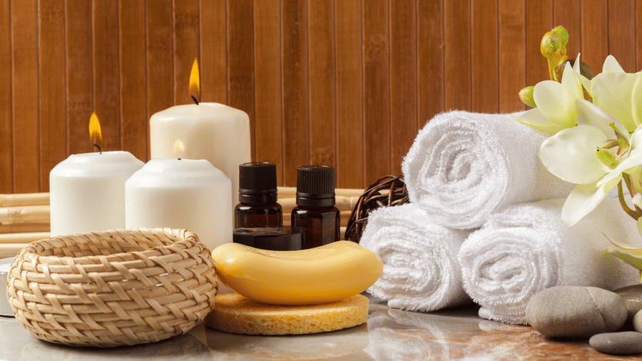 A table with towels beautifully wrapped and placed next to candles alongside two bottles of essential oils, and other utilities.