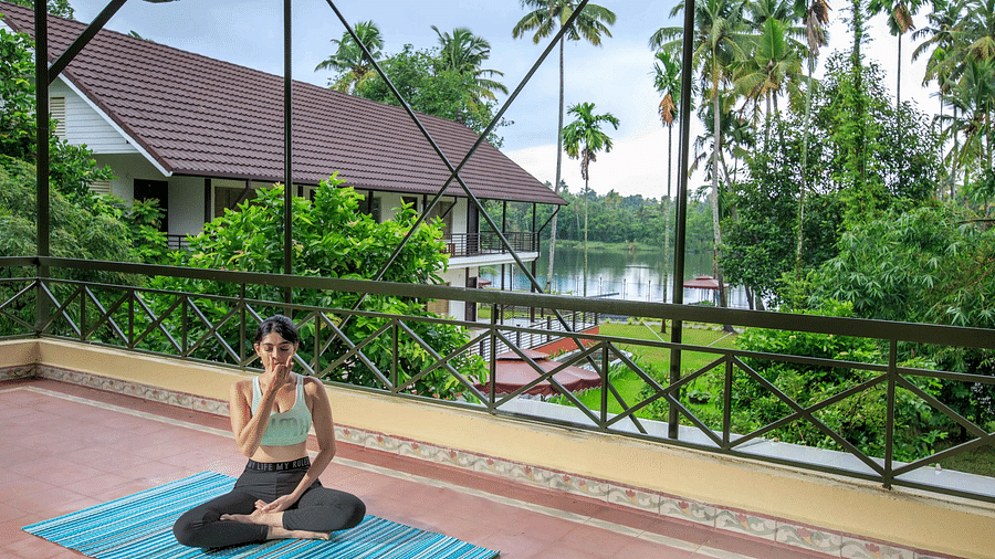 A yoga mat and props on a balcony overlooking a body of water and greenery, with a building visible in the distance.