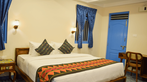 A hotel room with a double bed, blue accents, and traditional Indian textile patterns - Ibex Resorts, Coimbatore (Kakarla)