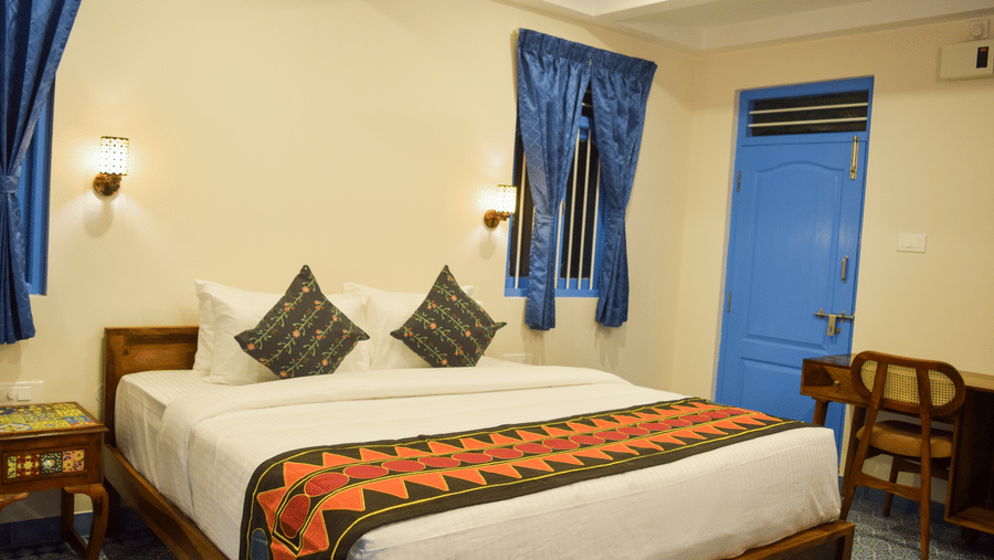 A hotel room with a double bed, blue accents, and traditional Indian textile patterns - Ibex Resorts, Coimbatore (Kakarla)