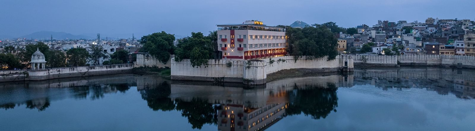 the facade of Hotel Rajdarshan, Udaipur with a lake surrounding it.