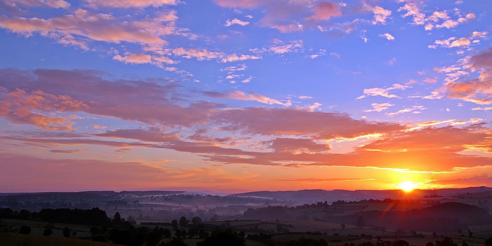 An aerial view of a breathtaking sunrise over a mountain range, with vibrant colours lighting up the sky, creating a stunning natural landscape.