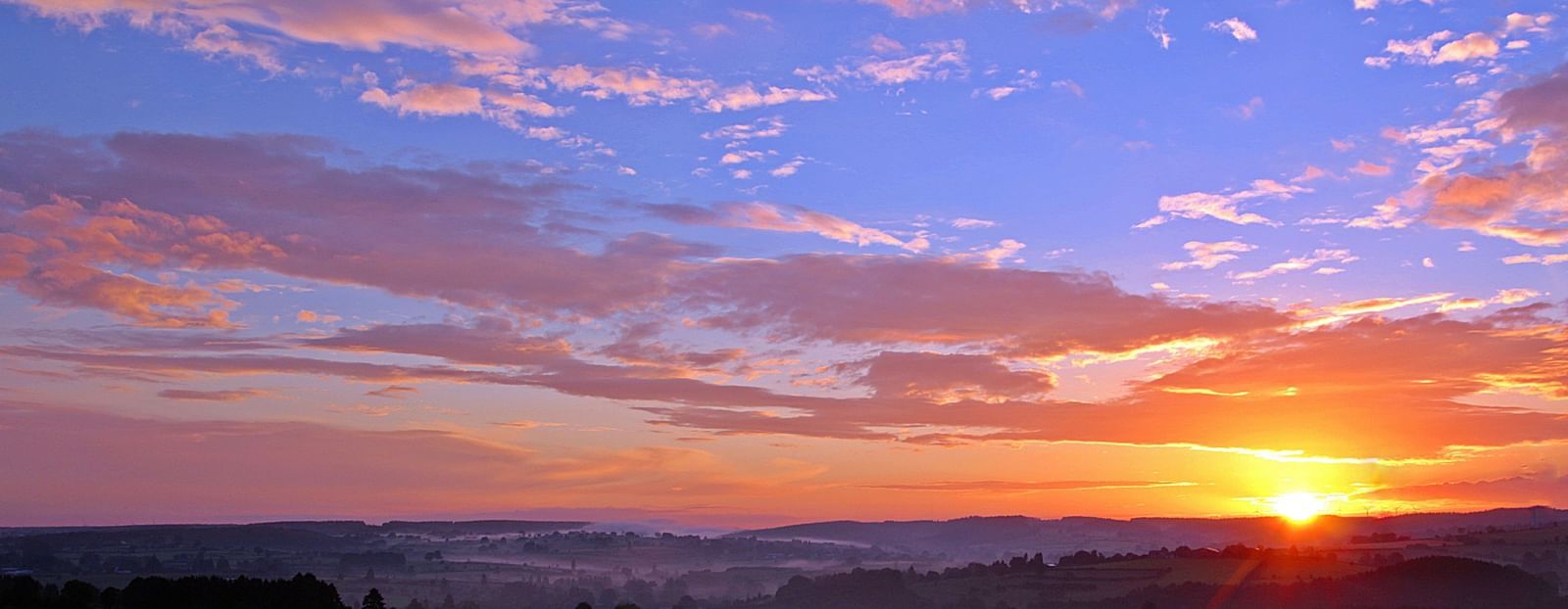 An aerial view of a breathtaking sunrise over a mountain range, with vibrant colours lighting up the sky, creating a stunning natural landscape.
