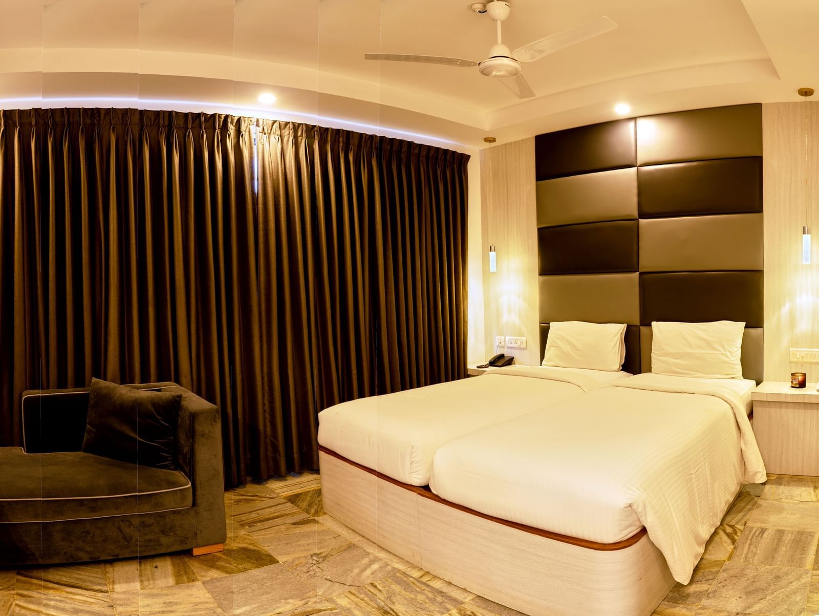 A comfortable and modern hotel room at Hotel Mamallaa Heritage, featuring a large bed with white linens, a television, and dark curtains.