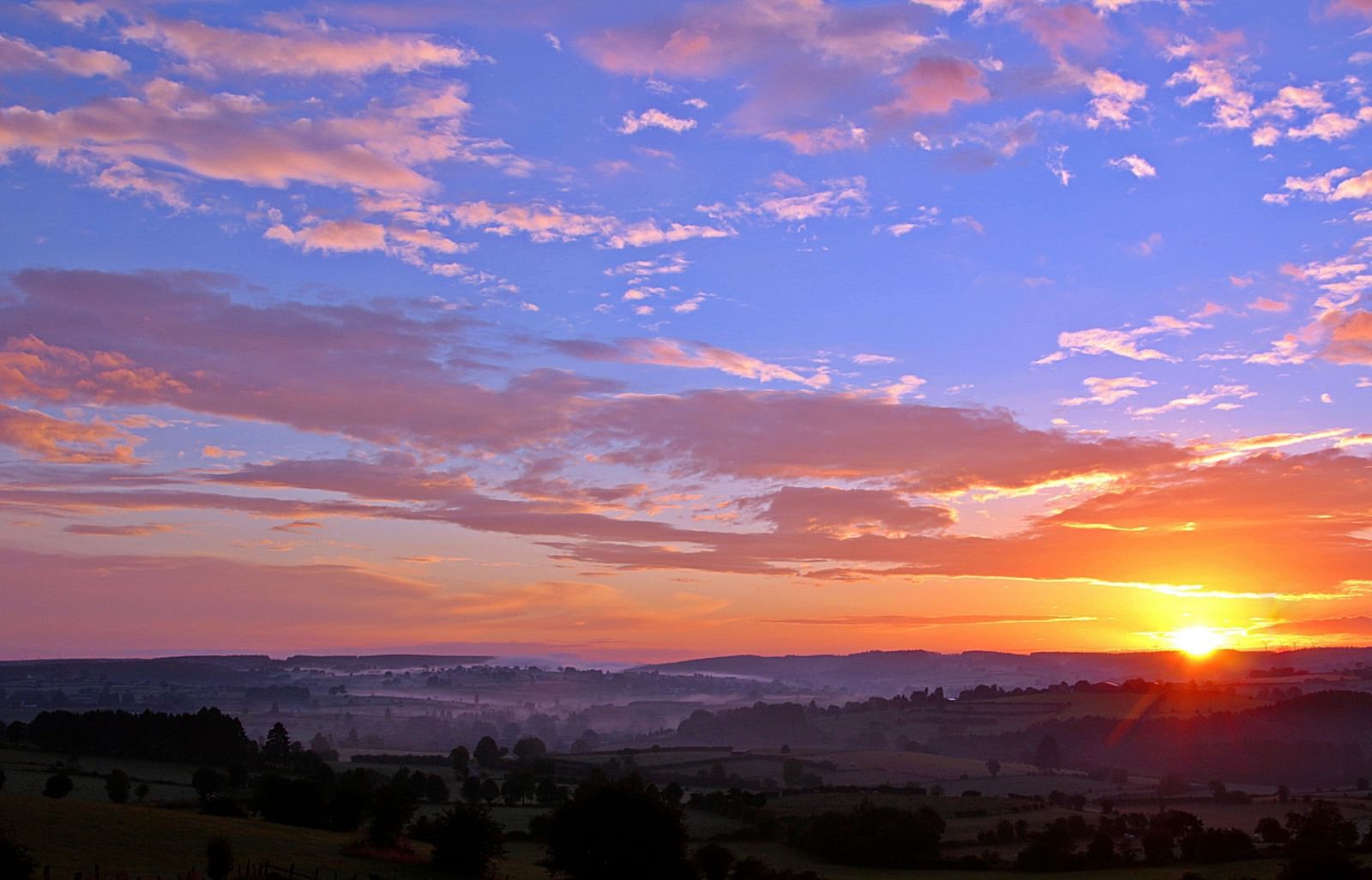 An aerial view of a breathtaking sunrise over a mountain range, with vibrant colours lighting up the sky, creating a stunning natural landscape.