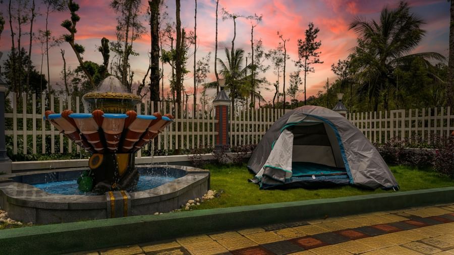 A shot of the fountain and decorative rock structure in the garden at Bhuthanakadu Retreat, with a vibrant, colorful sunset in the background.
