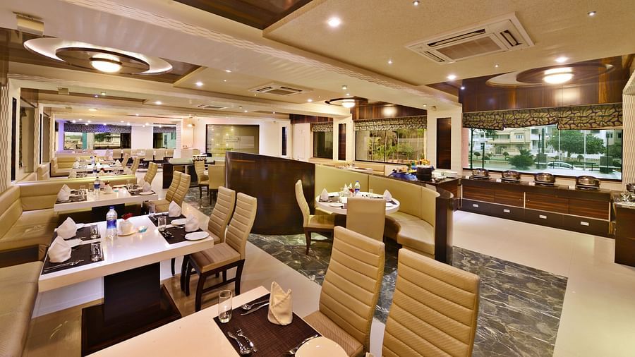 A spacious hotel restaurant, likely at Lords Inn Porbandar, with multiple tables and chairs arranged for dining.