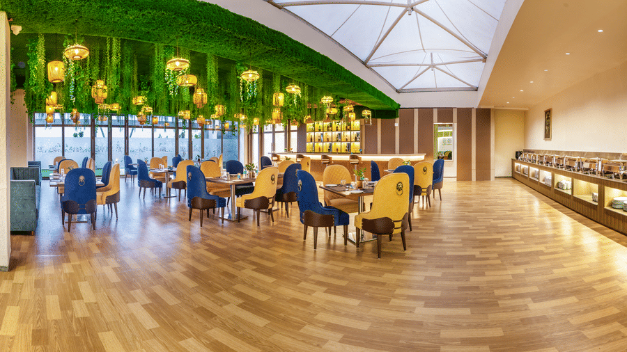 Bright restaurant at Lords Inn Sangam, Bhopal featuring a skylight ceiling, blue and wooden chairs, dining tables, and warm wooden flooring.