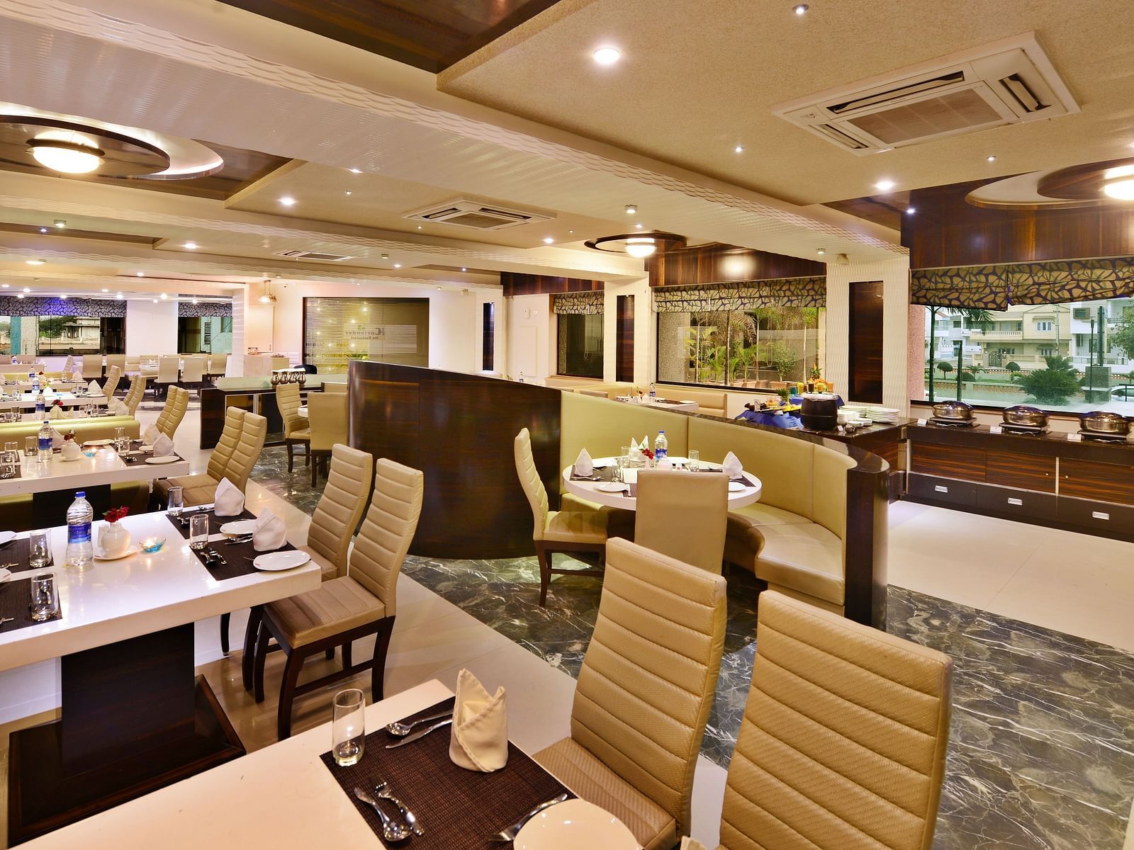 A spacious hotel restaurant, likely at Lords Inn Porbandar, with multiple tables and chairs arranged for dining.