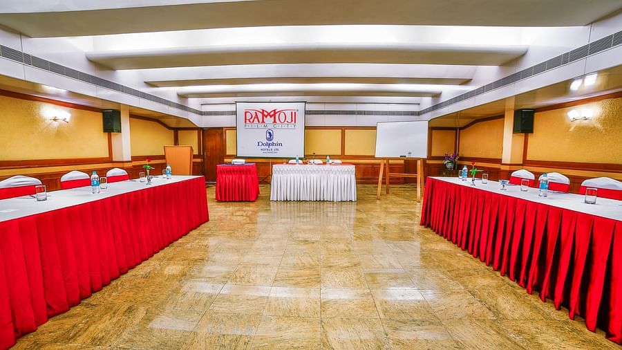 A conference room with red draped tables arranged facing a white presentation board - Tara, Comfort Hotel in Hyderabad - Ramoji Film City.