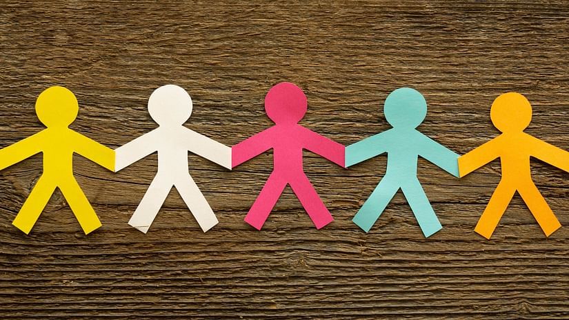A row of colourful paper cut-out figures holding hands against a wooden background.