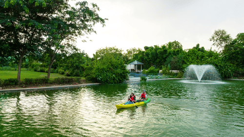 A couple boating in a lake at Karma Lakelands amidst lush greenery.