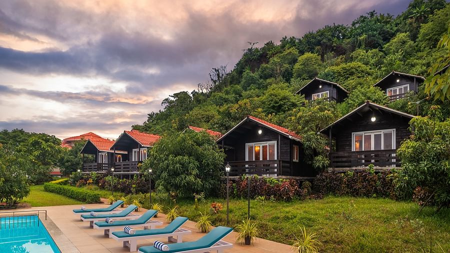 A pool surrounded by lush greenery and cottages used for accommodations - Highland Sarovar Portico, Sindhudurg.