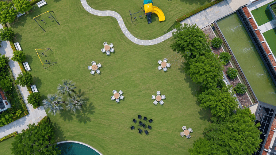 An overhead view of a lawn at Hotel Sonar Bangla, Mayapur, featuring outdoor seating arrangements, a slide, and paved pathways.