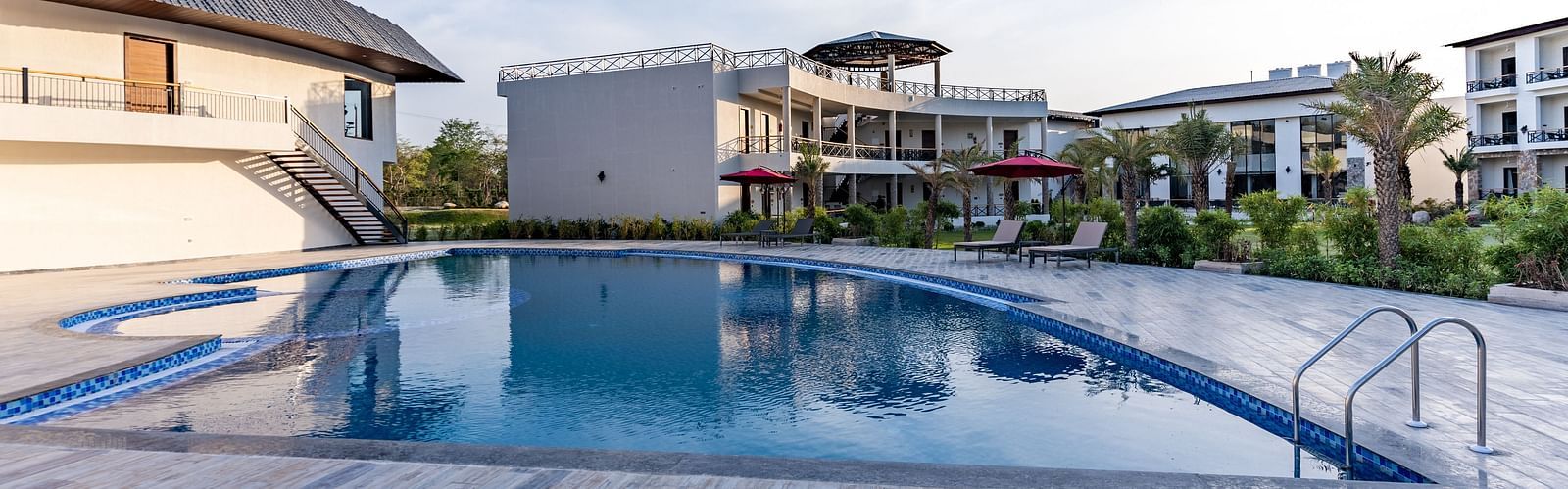 A well maintained swimming pool in front of our hotel rooms seen on a sunny day - Shervani Pebbles & Pines, Corbett