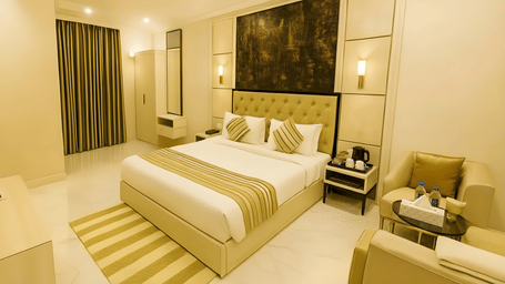 A well-lit guest room at Hotel Apple Park Delhi with a large bed, striped rug, olive green curtains, and a seating area with tan armchairs