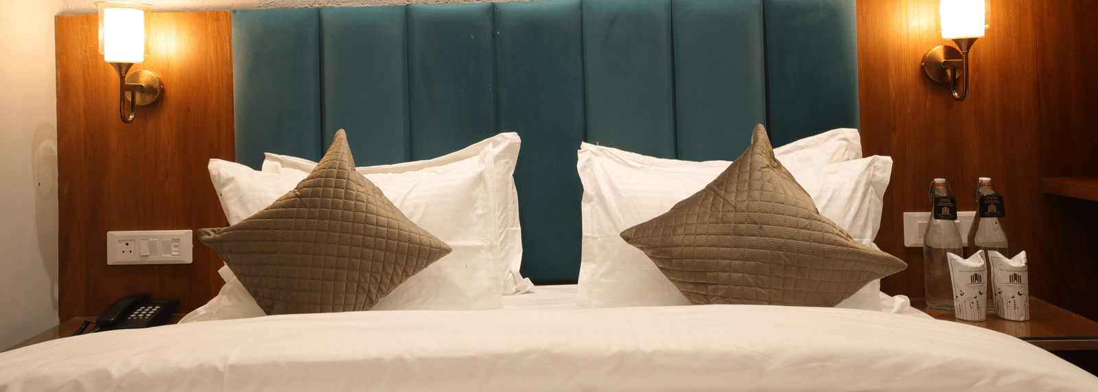 A bedroom with a king size bed with linens, cushions, and wall lamps at Perfectstayz Premium Laxmi Heritage.