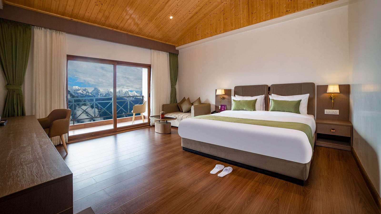 Spacious hotel room with a large bed, wooden flooring, vaulted wooden ceiling, seating area, and a sliding glass door offering a scenic mountain view - Yashshree Pelling Chekhim Retreat.
