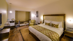 Deluxe Twin Room at Pride Premier Bengaluru featuring a double size bed, bedside table on either side, work desk and chair, flat TV screen, and sofa chair.