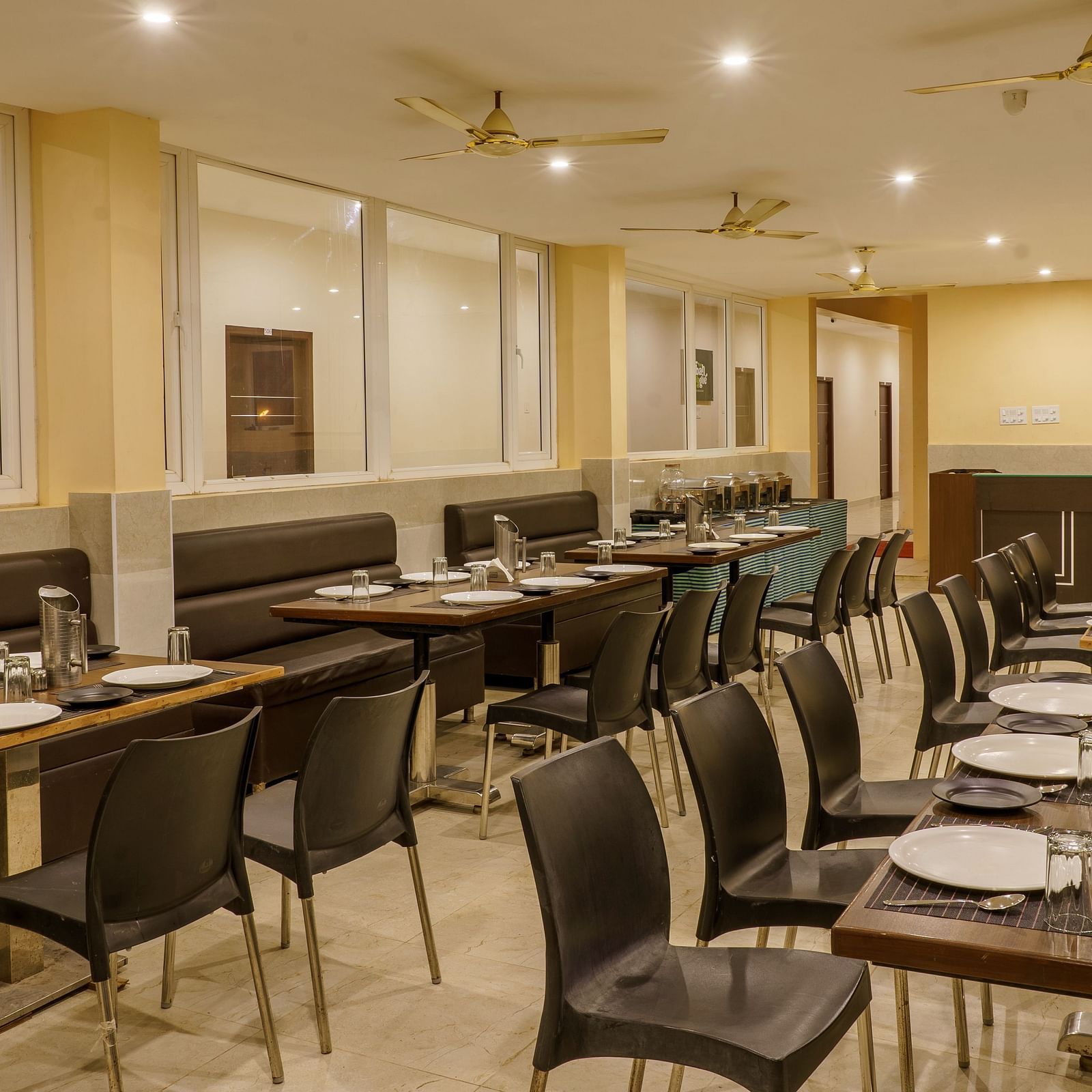 Dining area at Wyt Hotels Rameswaram featuring chairs and table with cutlery set. On the ceiling there are fans and lights.