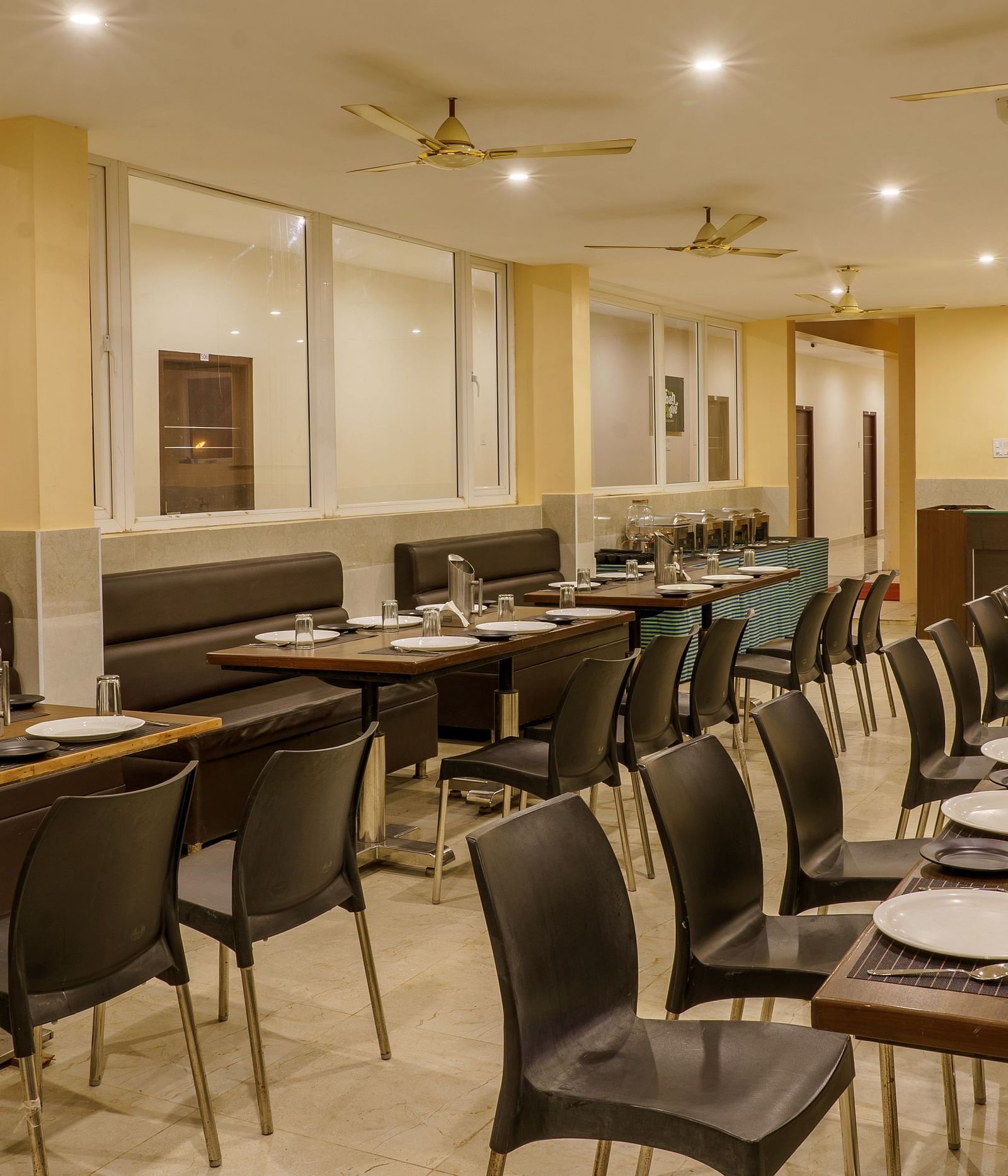 Dining area at Wyt Hotels Rameswaram featuring chairs and table with cutlery set. On the ceiling there are fans and lights.