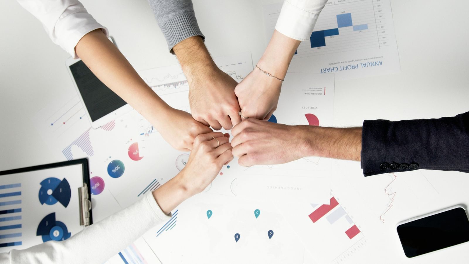 Five hands together over a table with papers