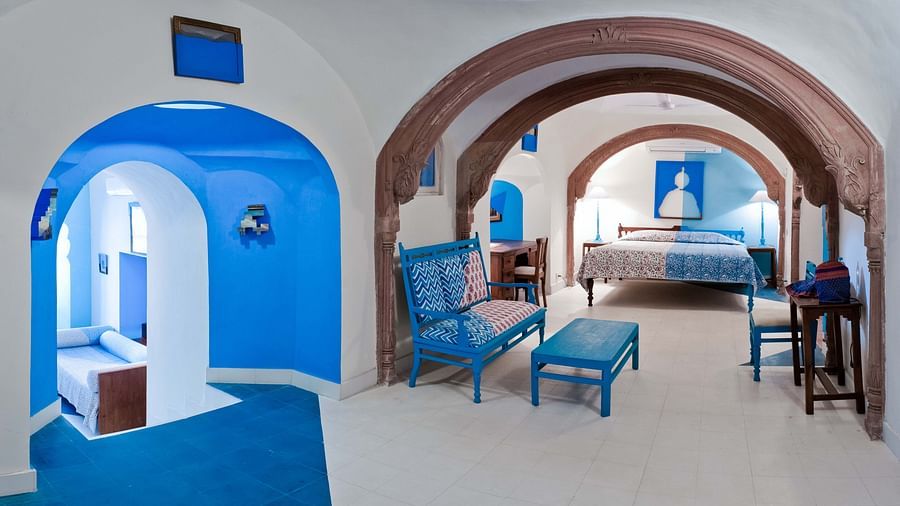 A hotel suite with arched doorways connecting different areas, including a blue-themed room with a daybed, a seating area with blue furniture, and a bedroom with a bed at Tijara Fort-Palace - 19th Century, Alwar.