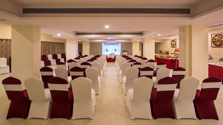A spacious hotel hallway is lined with neatly arranged chairs draped with white and red fabric - Lords Inn Vadodara