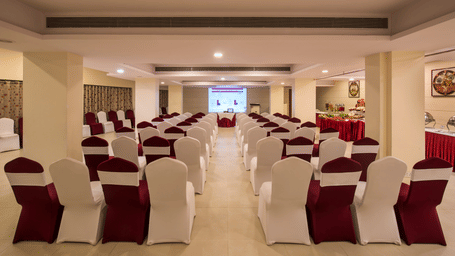 A spaciously decorated banquet hall in Vadodara with neatly arranged chairs draped with white and red fabric — perfect for any events at Lords Inn.