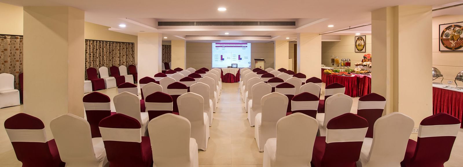 A spacious decorated banquet hall with neatly arranged chairs draped with white and red fabric at Lords Inn Vadodara.