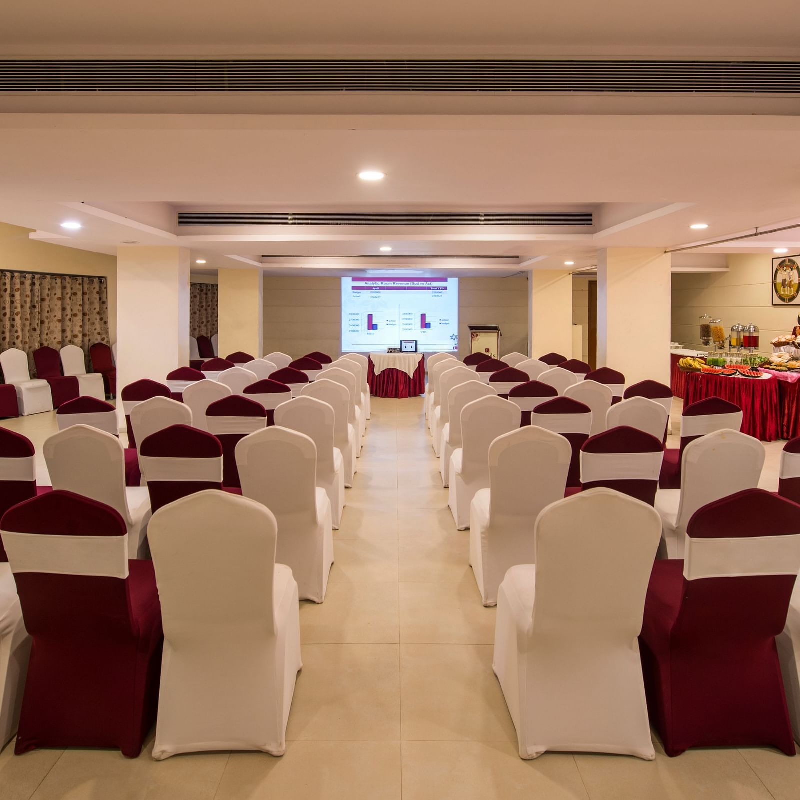 A spacious decorated banquet hall with neatly arranged chairs draped with white and red fabric at Lords Inn Vadodara.