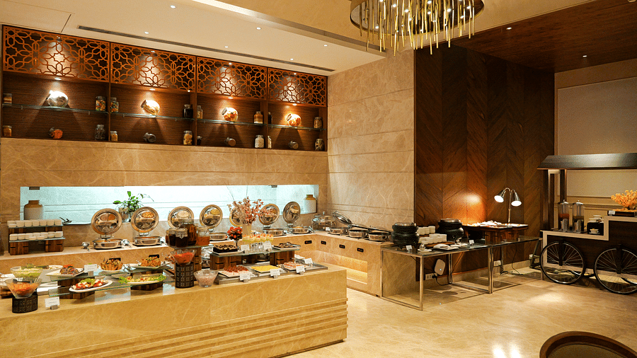  A well-lit buffet area within The Gaurs Sarovar Premiere, featuring a variety of dishes attractively presented. Serving stations and guests selecting food are visible.