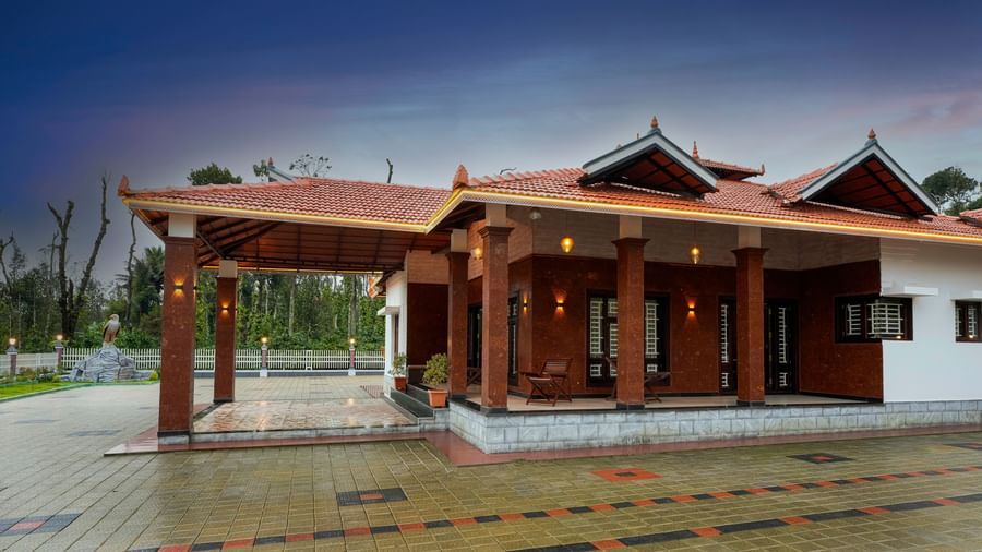 An evening shot of the main building at Bhuthanakadu Retreat, highlighting the traditional architecture and a wet, reflecting courtyard under a twilight sky.