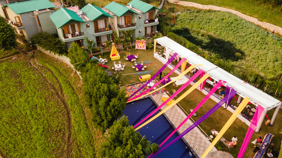 Aerial view of Corbett Nirvana Resort showing a poolside area covered with a vibrant pink and yellow draped canopy setup for an event, with the resort rooms in the background.