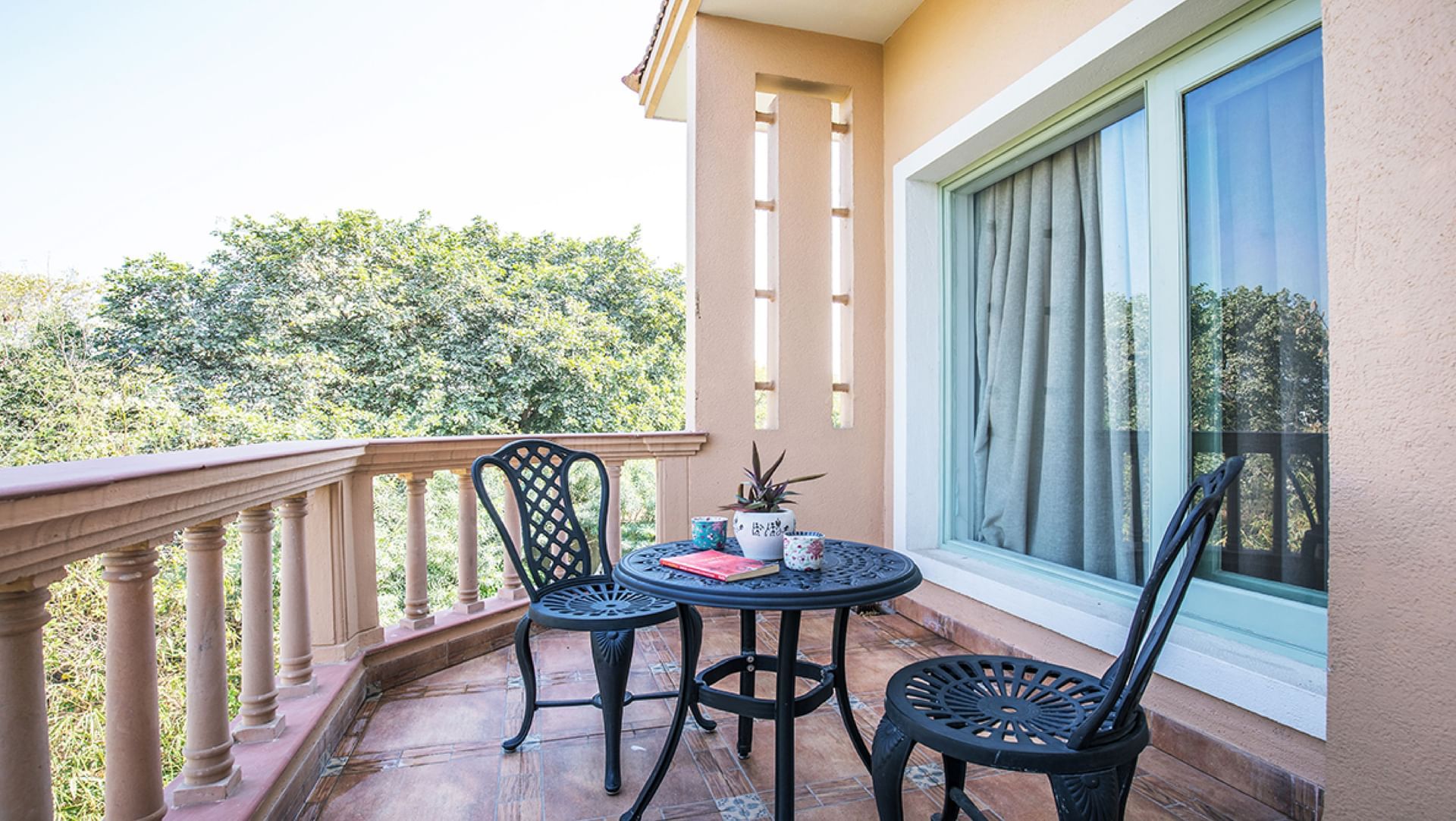 Balcony seating with a round table, chairs, potted plant, and mugs overlooking greenery at Karma Chalets.