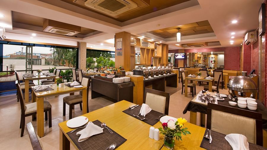A bright hotel dining area with wooden tables, chairs, and buffet setup - Lords Eco Inn Dahej