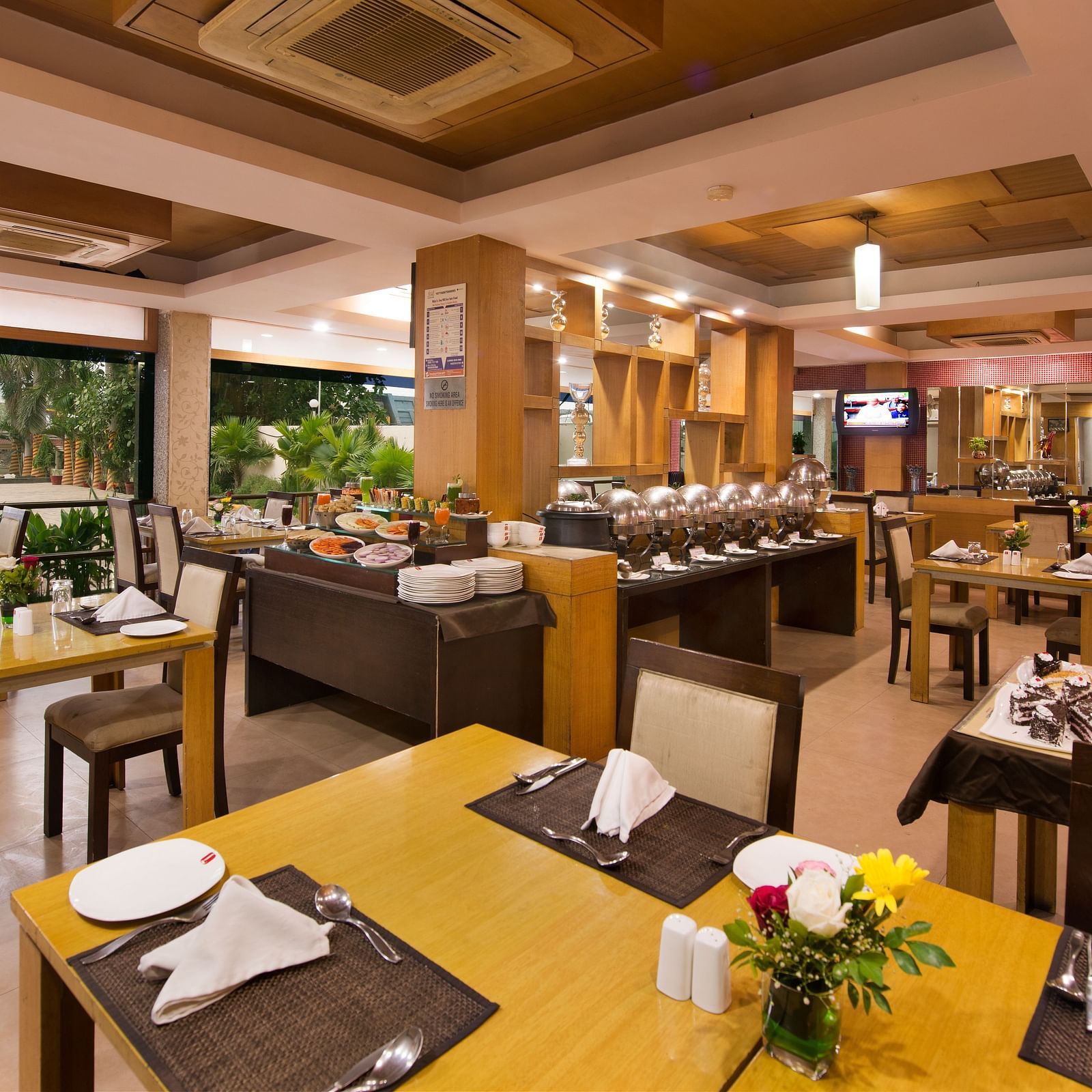 A bright hotel dining area with wooden tables, chairs, and buffet setup - Lords Eco Inn Dahej