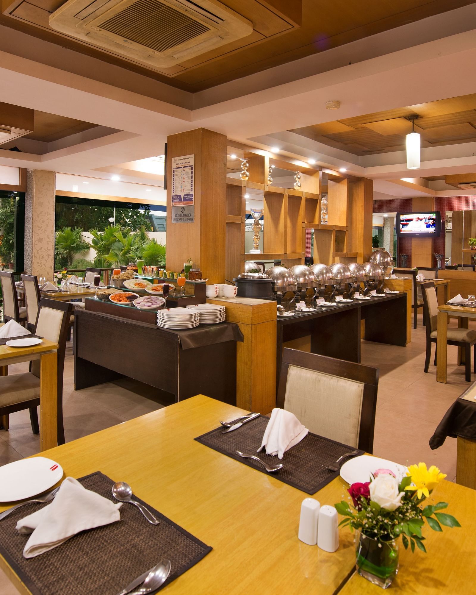 A bright hotel dining area with wooden tables, chairs, and buffet setup - Lords Eco Inn Dahej